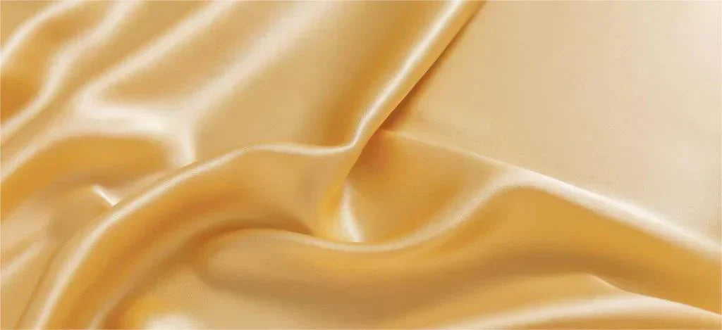 Luxurious golden mulberry silk fabric with smooth, flowing drapes and a characteristic lustrous sheen, showcasing the premium textile's natural elegance and soft folds typical of high-quality silk material