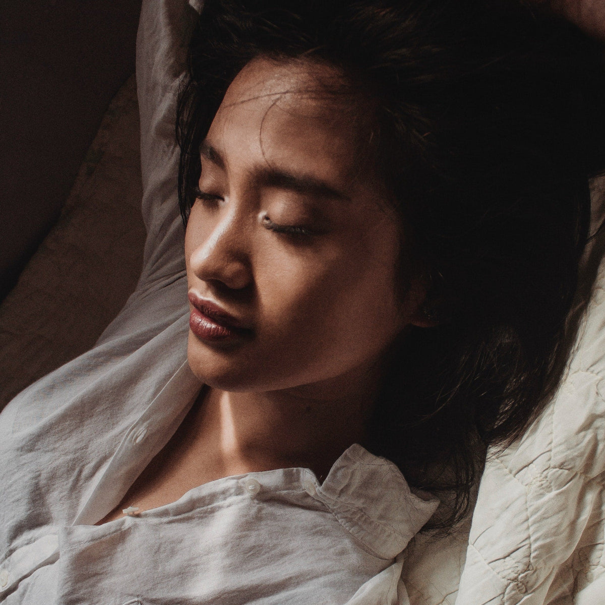 Close-up of a woman with eyes closed peacefully resting or sleeping in bed with soft light on her face