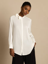[White] White long-sleeve collared blouse with black wide-leg trousers in a front crop to thighs, one hand tucked into a pocket. 001