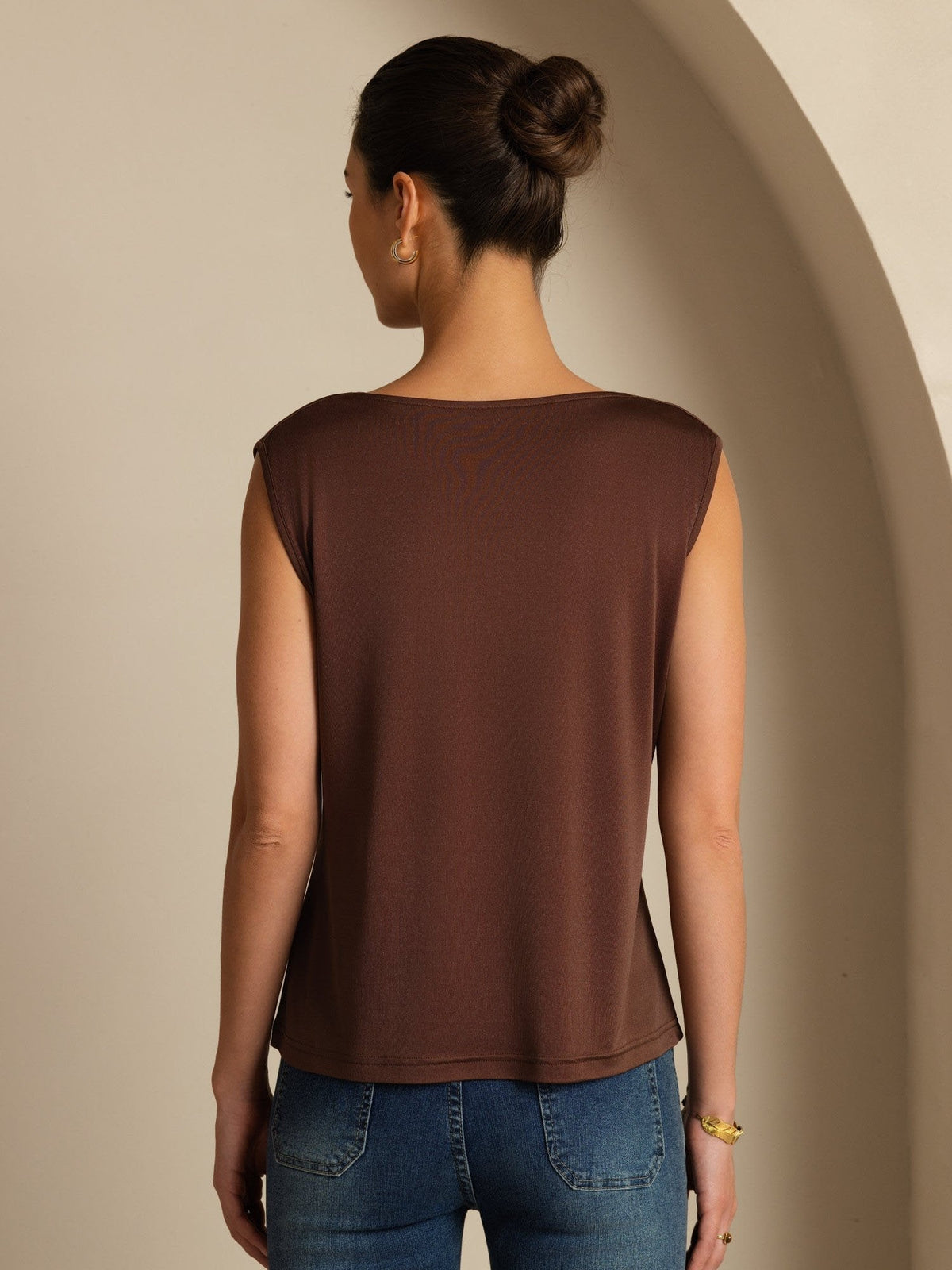 [Coffee] Rear studio view of a model wearing a coffee-brown sleeveless cowl-neck top with blue jeans. 002