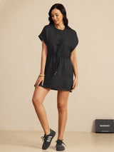 [Black] black cap-sleeve short dress with drawstring waist and pockets, full front view, model standing with one knee bent. 006