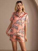 [Pink Cat] Peach pink cat-print short pajama set with contrast piping, three-quarter front view, one hand lifting the top hem. 003