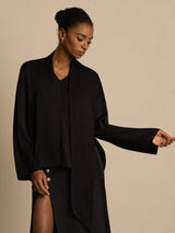 [Black] Black draped-neck long-sleeve blouse with a black skirt in an angled view, with the model turned. 003