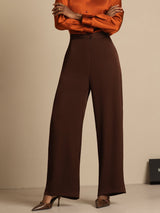 [Bitter Chocolate] Brown wide-leg trousers with a rust-orange blouse in a front waist-to-shoes view, crossed arms above the trousers. 003