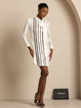 [White] Frontal view: white long-sleeve tunic mini dress with vertical black stripes, with one hand placed at the waist. 007