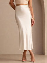 [Beige] Cream glossy maxi skirt on a model in a waist-to-ankle front crop with one foot crossed ahead of the other. 003