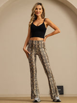 [Snakeskin] Front view of gray-brown snakeskin flared trousers with one hand at the hip and chunky sneakers visible. 006