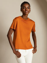 [Orange] Front upper-thigh view of an orange short-sleeve top with white trousers and both elbows bent. 006