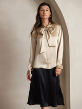 [Champagne] Champagne beige long-sleeve blouse with a large tie-neck bow, full front view, model standing with both arms relaxed. 001