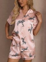 [Pink Zebra] Front waist-up view of a silk short-sleeve pajama set with shorts in pale pink with small dark animal motifs 004