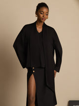 [Black] Black draped-neck long-sleeve blouse with a black skirt in a front crop to thighs, the skirt continuing below the frame. 005