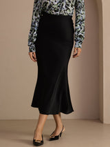 [Black] Black glossy maxi skirt on a model in a waist-to-ankle front crop with one foot crossed ahead of the other. 001
