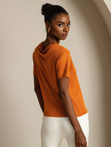 [Orange] Rear studio view of a model wearing an orange short-sleeve crew-neck top with white trousers. 002
