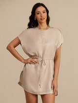 [Tan] light tan cap-sleeve short dress with drawstring waist and pockets, waist-up view, model with one hand on the hip. 004