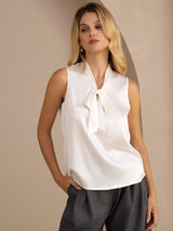 [White] White sleeveless tie-neck top in a front thigh crop, looking sideways with one hand in a pocket. 001