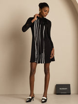 [Black] Black tunic mini dress with white stripes in a full-body front view, hand near collar, two-tone heels visible. 001