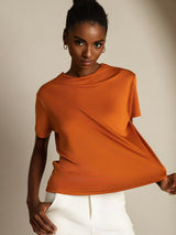 [Orange] Orange crew-neck top with white trousers in a front crop to hips, one hand pulls the hem sideways, the other on a thigh. 001