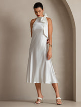 [White] White scarf-neck maxi dress in a full-body front view, one hand behind the back and the other lowered. 001