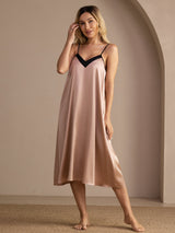 Blush pink V-neck nightgown with black trim, full front view with one hand beside her cheek.