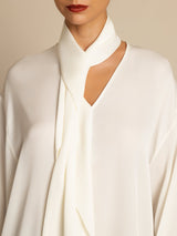 [White] Close studio view of a model wearing a white draped-neck long-sleeve blouse with dark brown wide-leg trousers. 005