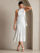 [White] Full front view of a white scarf-neck midi dress, with crossed ankles and one hand behind the neck. 007