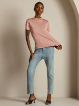 [Pink] Full front view of a blush-pink short-sleeve top with one hand pulling the hem and light blue jeans. 004
