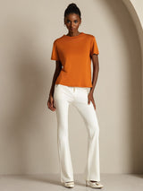 [Orange] A straight front view shows orange crew-neck top with white trousers, distinguished by one hand held at the waist. 007