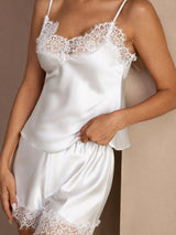 [White] White lace-trim camisole and ruffled shorts set in a lower close-up showing scalloped lace and nearby fabric. 004