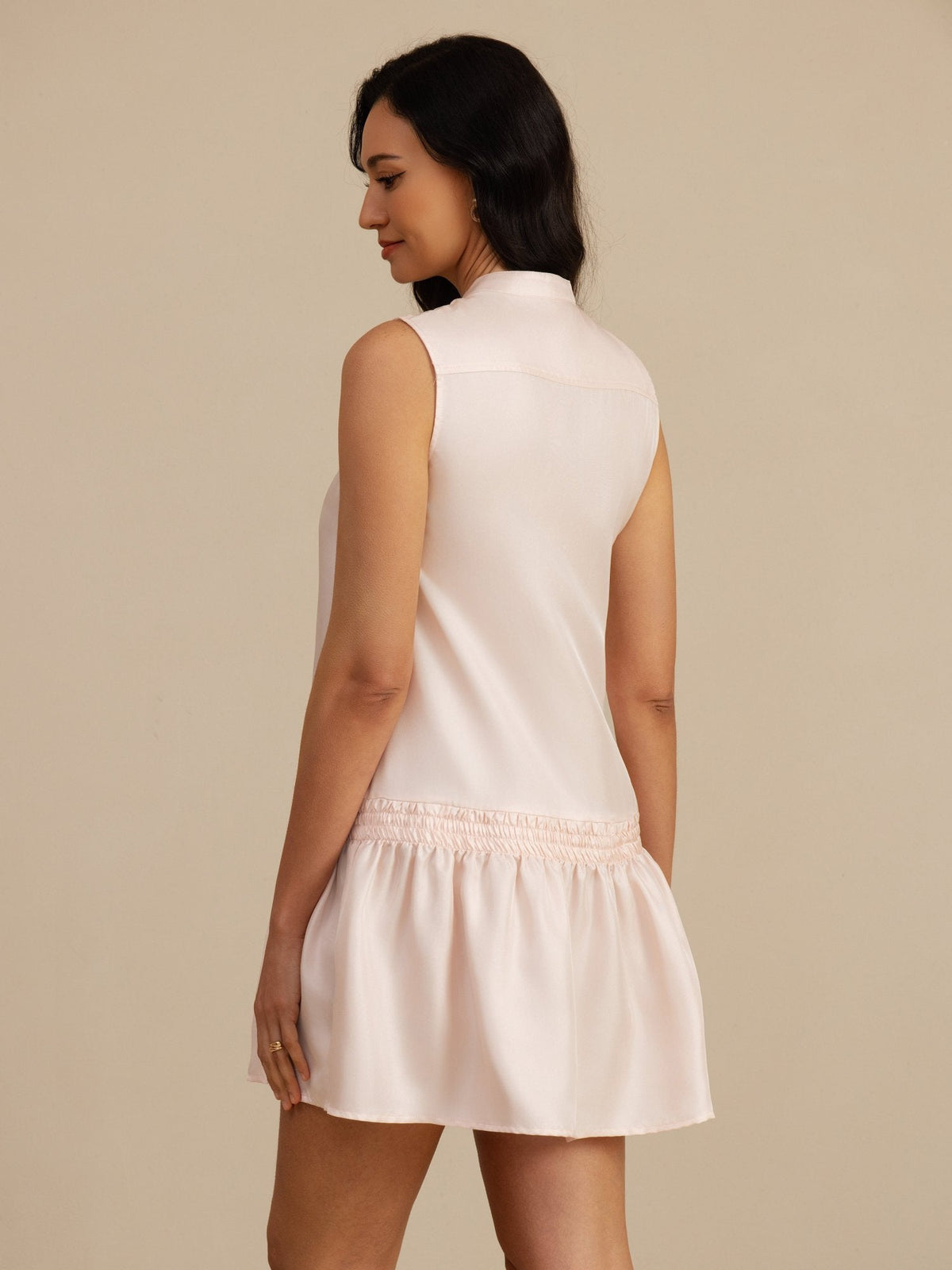 [Pink] Rear studio view of a model wearing a blush-pink sleeveless drop-waist mini dress with a gathered ruffle hem. 002