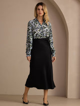 [Black] Black glossy maxi skirt in a full front view, with the model's arms down and feet set apart. 006