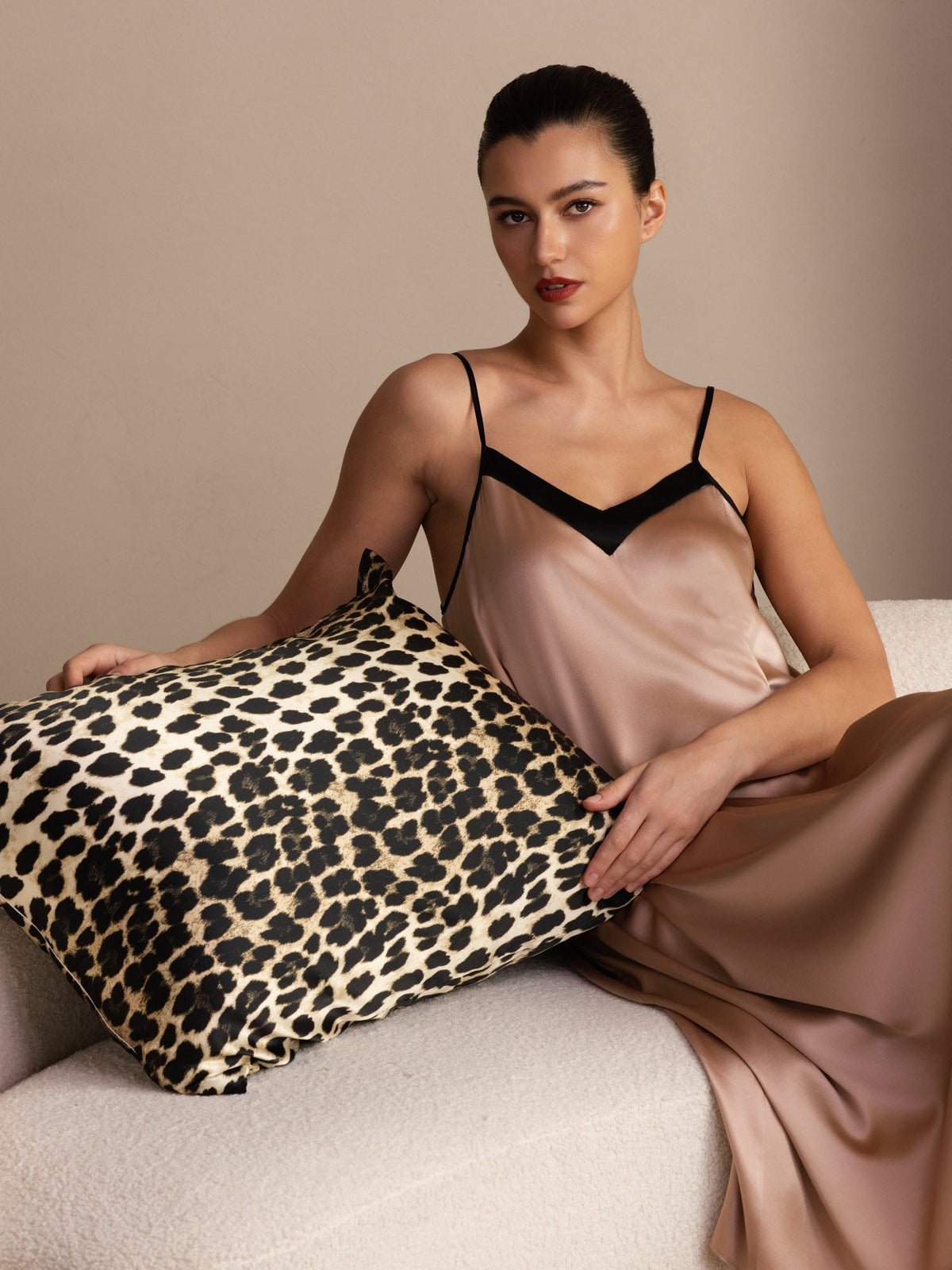 [Leopard] Tan, black and brown leopard-print square pillowcase, seated product view, pillow held flat across the model's lap. 001