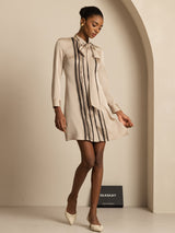 [Tan] Front view: beige long-sleeve tunic mini dress with vertical dark stripes, with one hand at the waist. 007