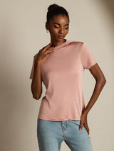 [Pink] Blush-pink crew-neck top with light blue jeans in a front crop to upper thighs, one hand at chest, the other at hip. 005