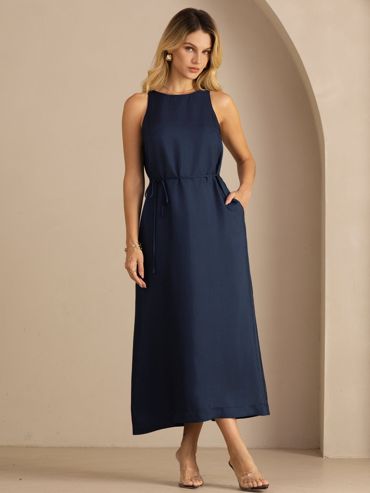 [Dark Blue] navy blue sleeveless scoop-neck midi dress, gathered waist and side pockets, full front view, model looking down. 001