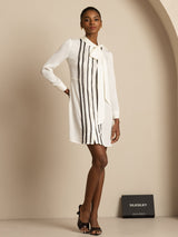 [White] Head-to-toe stance: white long-sleeve tunic mini dress with vertical black stripes, with weight held on one leg. 006