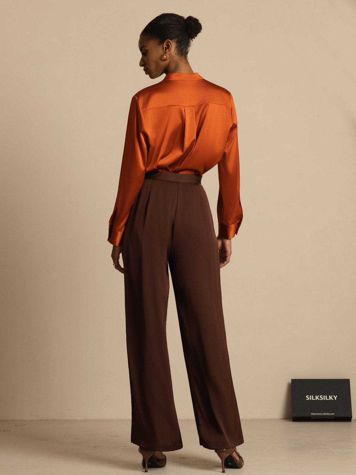 [Bitter Chocolate] Angled studio frame: brown high-rise wide-leg trousers with a rust-orange blouse, with the body facing one side. 002
