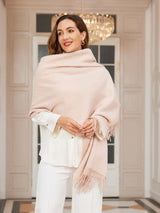 [Beige] very pale pink rectangular shawl with fringed edges, styled front view, over shoulders, hand at edge. 003
