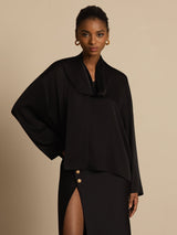 [Black] A mid-length frontal view shows black draped-neck blouse with a black skirt, with one arm bent at the model's side. 001