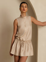 [Tan] Tan drop-waist mini dress with ruffle hem in a front crop to thighs, one arm extended sideways and the other lowered. 003