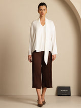[White] White draped-neck long-sleeve blouse with dark brown wide-leg trousers in a full front view, with the lower hem visible. 006