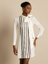 [White] White tunic mini dress with black stripes in a standing front crop to thighs, one hand at the hip and the other lowered. 004