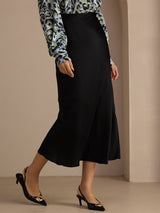[Black] Lower-body side studio view of a model wearing black glossy maxi skirt, showing the long skirt shape. 003