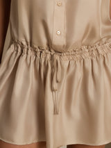 [Tan] Close studio view of a model wearing a tan sleeveless drop-waist mini dress with a gathered ruffle hem. 005