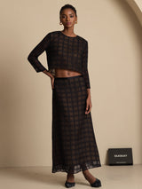 Model wearing a black textured grid pure silk high-waist A-line long skirt with sheer matching top