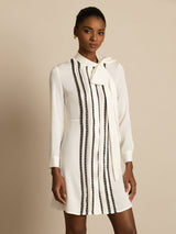 [White] White long-sleeve tunic mini dress with vertical black stripes in a front view cropped at the thighs, arms down. 001