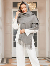 [Gray] medium gray rectangular shawl with fringed edges, styled front view, wrapped around the neck with hand at the temple. 001