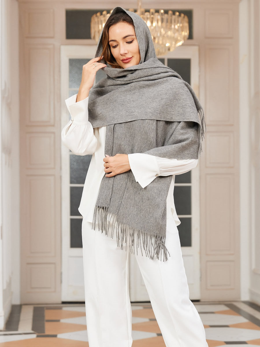 [Gray] medium gray rectangular shawl with fringed edges, styled front view, wrapped around the neck with hand at the temple. 001