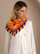 [Orange Dog] Close styled view of a 90 cm square silk scarf in orange, yellow, and red animal print with a dark striped border 003