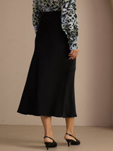 [Black] Three-quarter lower-body front studio view of a model wearing black glossy maxi skirt. 002