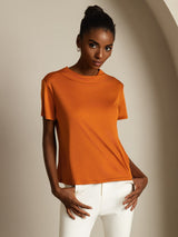 [Orange] The front of orange crew-neck top with white trousers fills a waist-up frame while the model keeps both arms lowered. 004
